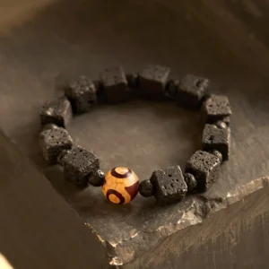 Lava Rock Dzi Bead Bracelet top-down flat lay featuring square and round black porous lava beads with central three-eye Dzi protection bead on natural stone surface