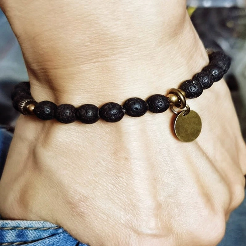 Lava rock healing bracelet worn on adult wrist in everyday setting, showing comfortable fit with dangling copper charm