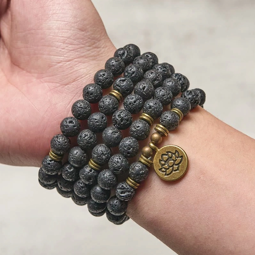 Lava rock mala worn on wrist as multi-wrap bracelet showing porous black beads and bronze lotus charm close-up