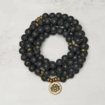 Lava rock lotus charm mala bracelet overhead view showing 108 black porous beads with bronze lotus pendant on light background