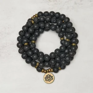 Lava rock lotus charm mala bracelet overhead view showing 108 black porous beads with bronze lotus pendant on light background