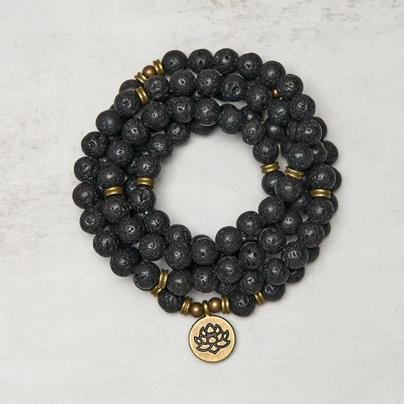 Lava rock lotus charm mala bracelet overhead view showing 108 black porous beads with bronze lotus pendant on light background