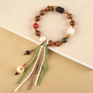 Lightning strike wood bodhi bracelet with cat paw charm and green tassel, flat lay on beige background showing mixed color beads and protective amulet design