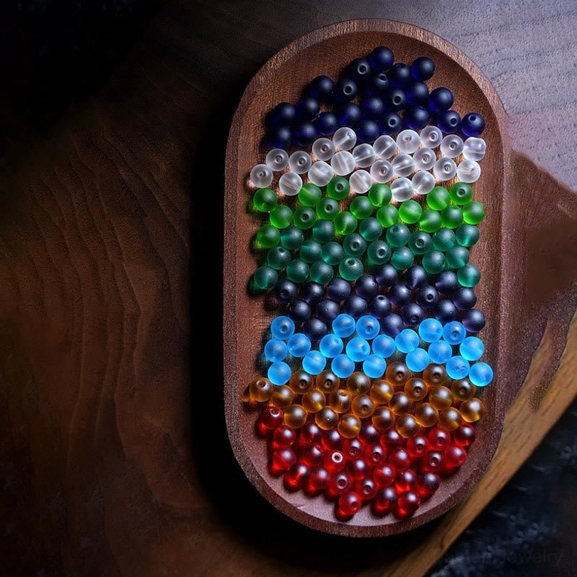Loose sorted frosted liuli glass beads in gradient rainbow colors arranged on wooden serving tray, overhead view