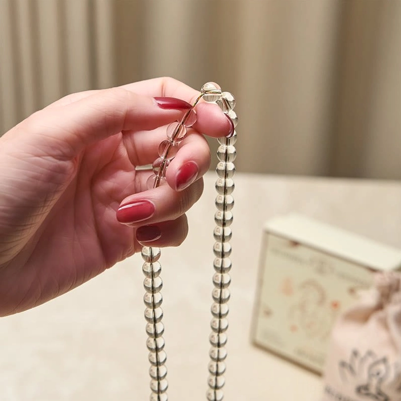 Single strand Liuli mala held between fingers showing clear beads and chakra colored end beads