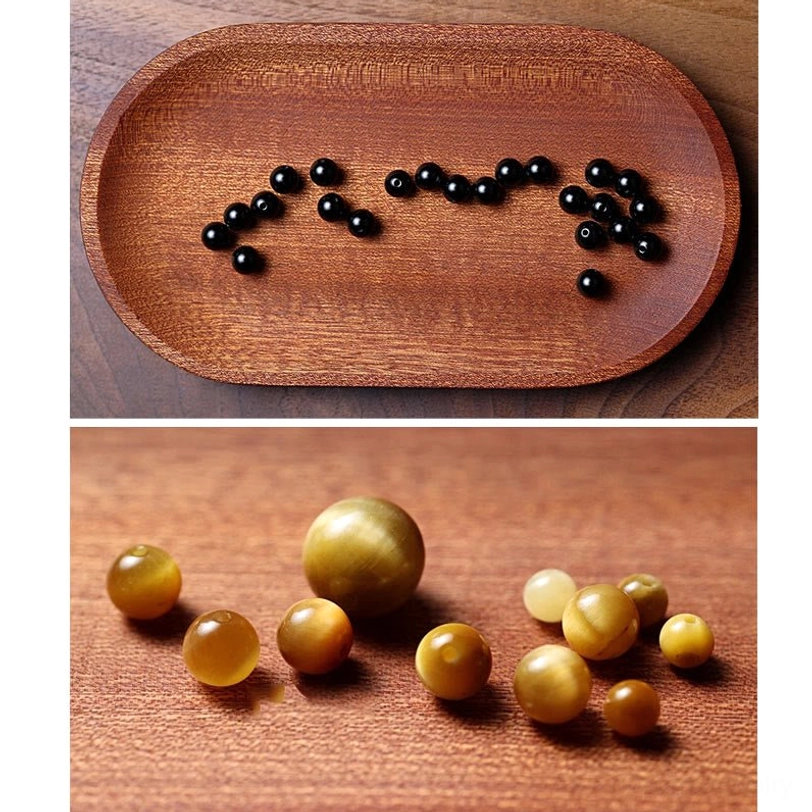 Loose black onyx and tiger eye mala beads scattered in dot arrangement on wooden oval tray, showing natural stone texture