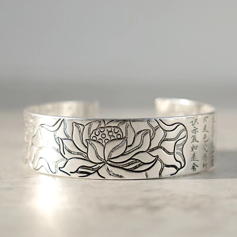 Open cuff bracelet with large engraved lotus flower and side sutra lettering, front eye-level view on gray surface