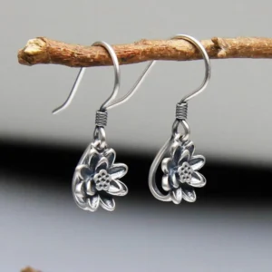 Lotus dangle earrings side angle view on wooden branch displaying wrapped earwire connection and lotus pendant profile