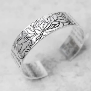 Handcrafted lotus bracelet showing detailed engraved lotus pattern and scripture on light gray background, three-quarter angle