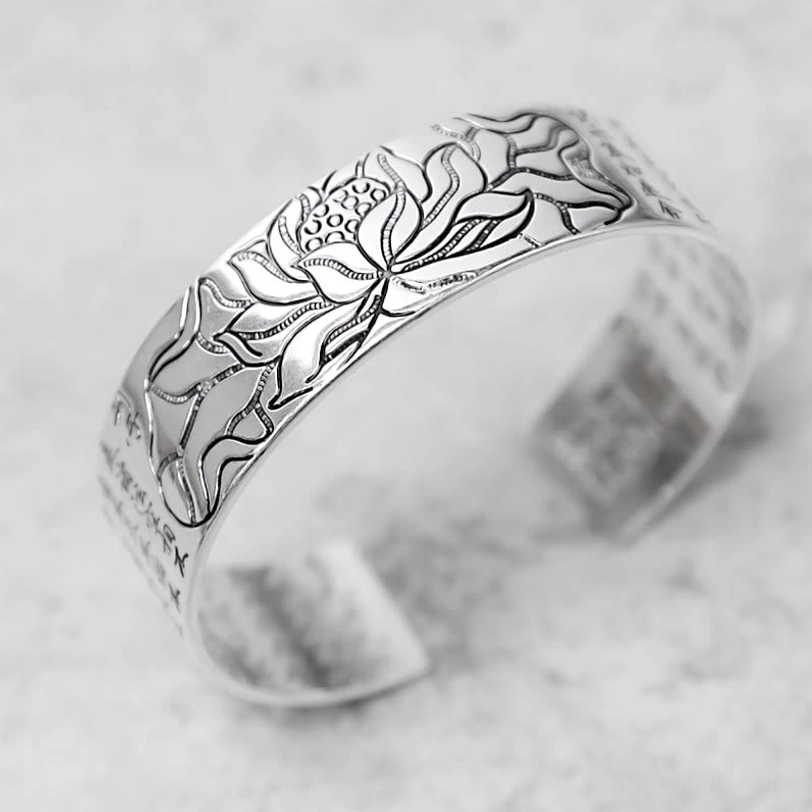 Handcrafted lotus bracelet showing detailed engraved lotus pattern and scripture on light gray background, three-quarter angle