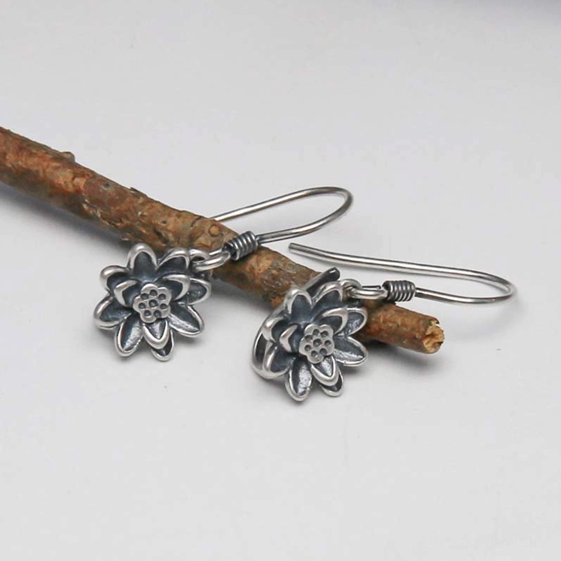 Pair of antiqued sterling silver lotus dangle earrings oblique view on wooden branch with gray background