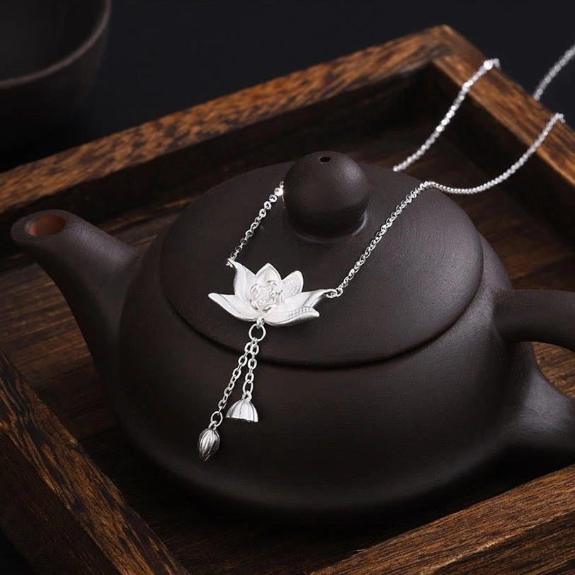 Sterling silver lotus pod pendant with graceful tassel design resting on oriental tea tray setting