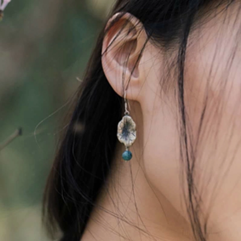 Side close-up of model wearing turquoise dangle earrings with lotus leaf pendant and outdoor floral backdrop