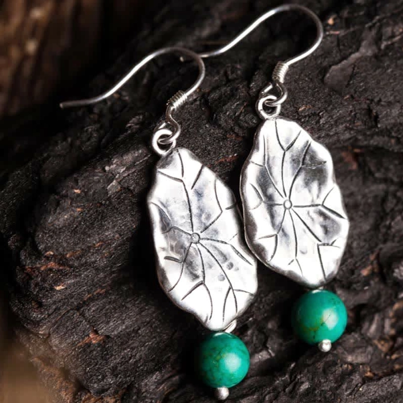 Close-up top view of turquoise lotus leaf dangle earrings with intricate veined pendant details on dark wood