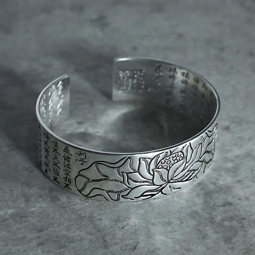 Open cuff bracelet with engraved lotus flower pattern and Chinese sutra text, low top-side view on matte background