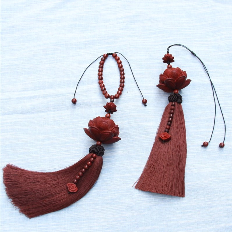 Two loose red sandalwood lotus tassel pendants on light blue fabric background displaying adjustable cords and cloud-shaped pendants