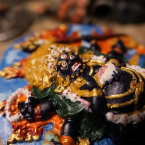 Side profile of Daikokuten Mahakala Buddha clay sculpture showing dynamic pose, vibrant multicolor paint, and gold decorative details