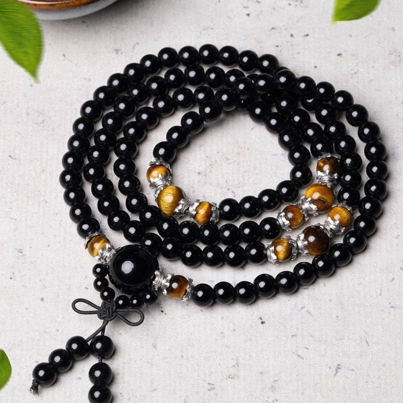 Flat-laid tibetan mala set with central focal bead and tassel pendant, styled with green leaf on dark table