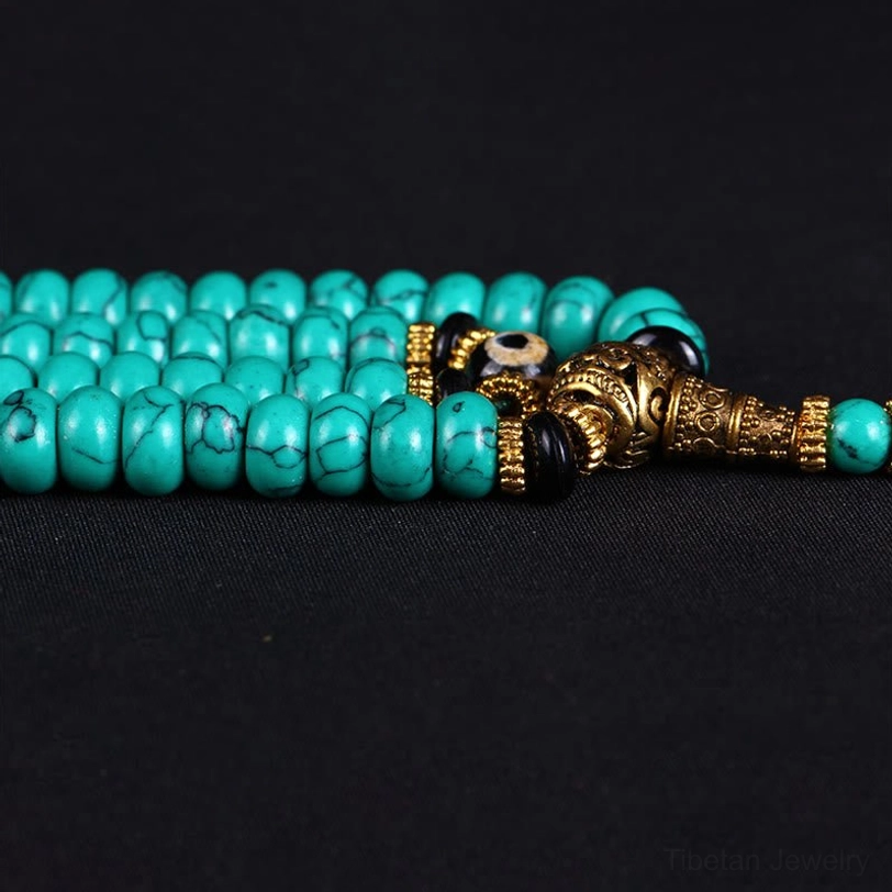 Close-up of mala bead components showing golden guru bead, turquoise barrel beads, and black spacer beads
