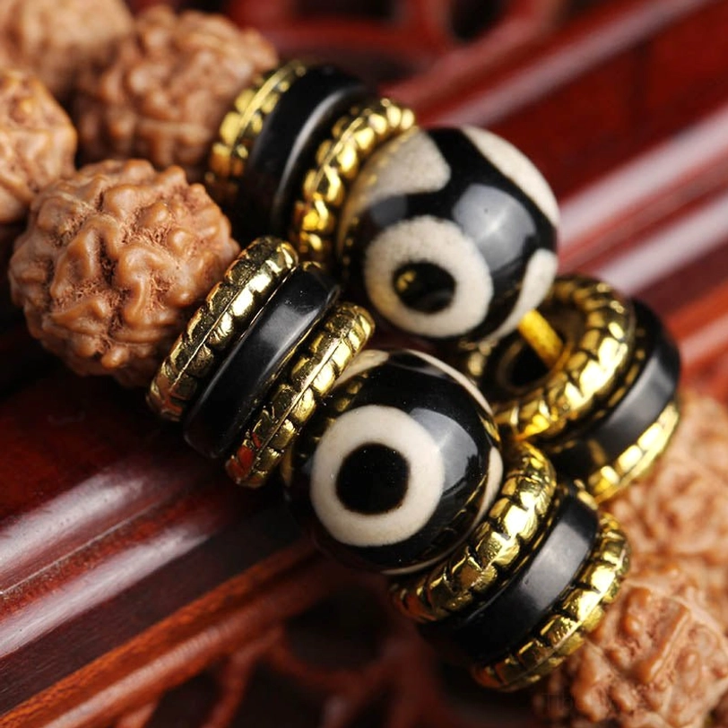 Close-up detail of 108 mala beads showing black-white dzi beads, gold-plated metal rings, and textured rudraksha seeds