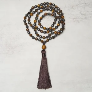 Circular arrangement of 108 Tiger Eye and Hematite prayer beads with tassel, centered flat lay view on gray surface
