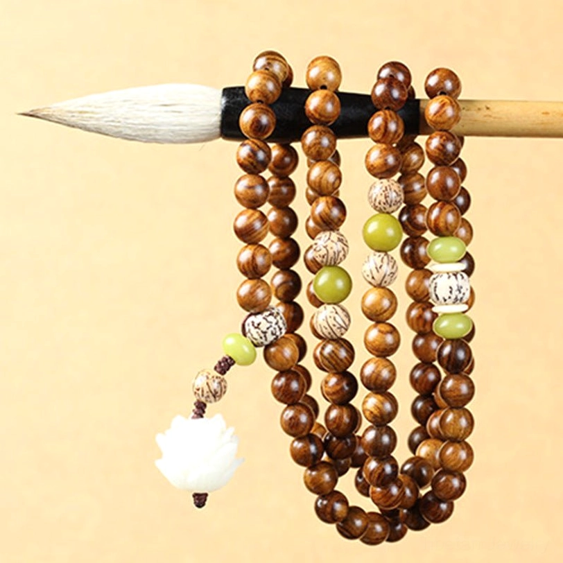 Tibetan prayer beads mala hung on Chinese calligraphy brush, showing lotus pendant and decorative patterned spacer beads