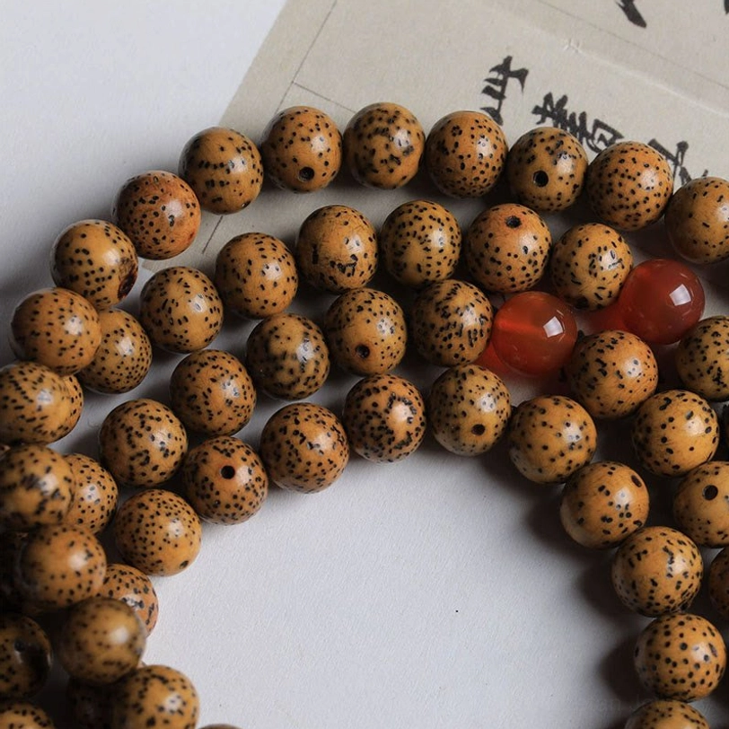 Partial Tibetan 108-bead mala with brown spotted bodhi seeds and red agate accent beads on plain background