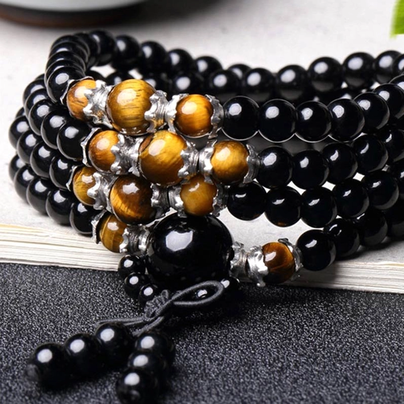 Close-up of 108 bead mala with large obsidian focal bead and metal spacer accents on wooden surface