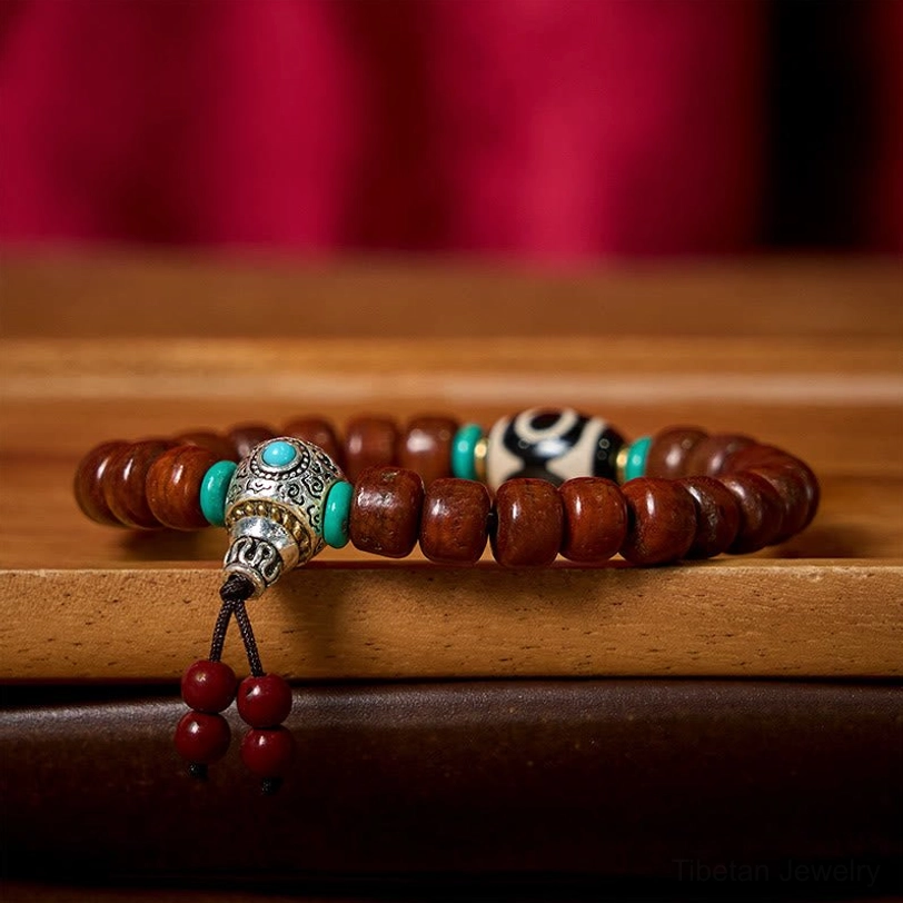 Tibetan mala bracelet with brown beads three-eye Dzi bead and red tassel on wooden table