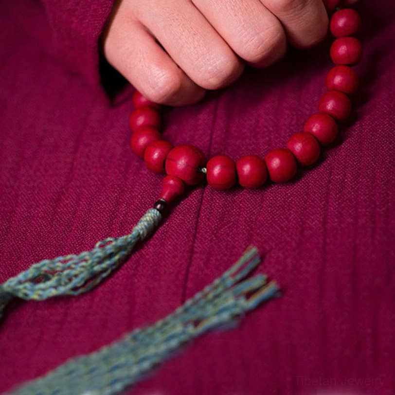 Top-down view of hand-held tibetan mala with loose teal woven tassel and round beads