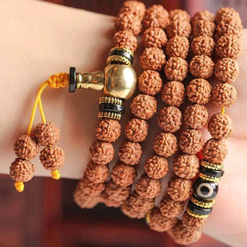Multi-layer worn mala bracelet close-up showing golden metal hardware, black dzi spacer beads, and hanging tassel pendant