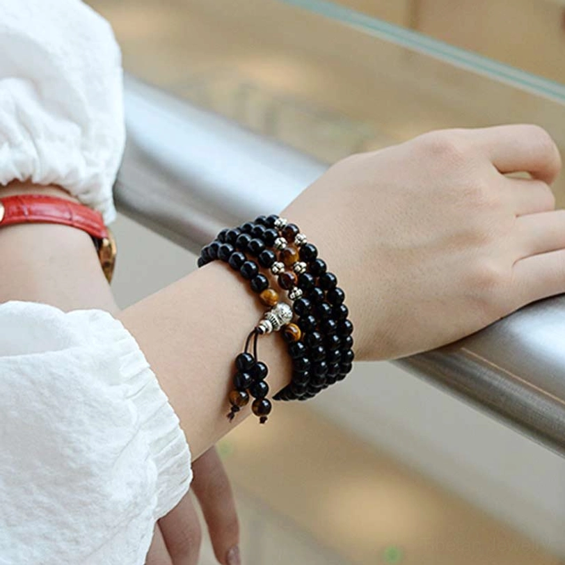 Black obsidian tiger eye mala bracelet worn on wrist, lifestyle shot showing daily wear styling on metal railing