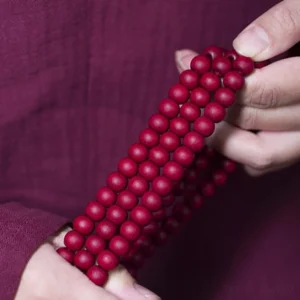 Close-up view of handmade mala prayer bead bracelet showing matte red wooden beads strung on premium cord with double tassel detail on maroon fabric