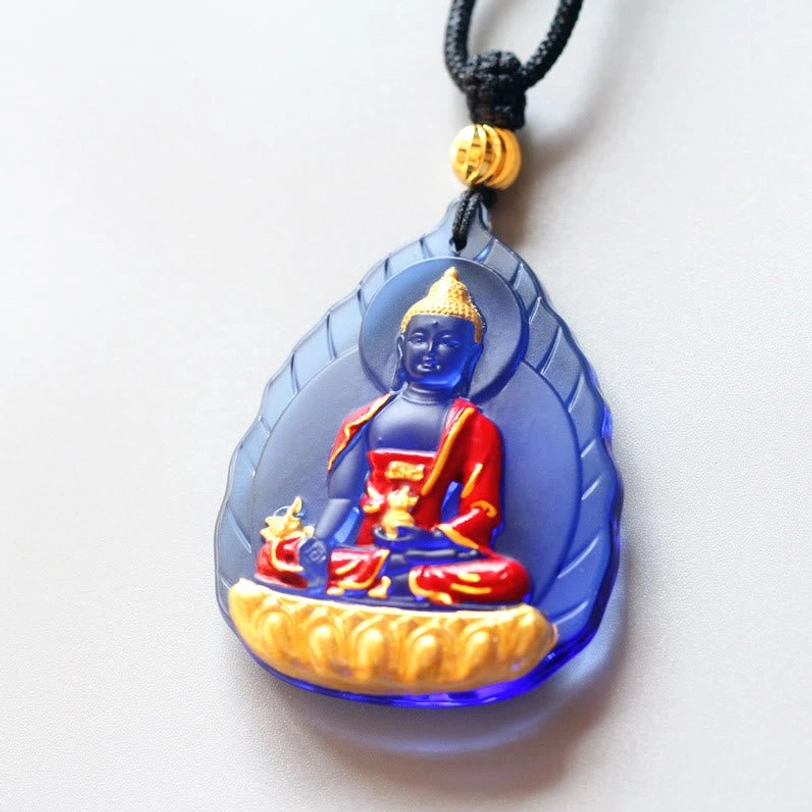 Tibetan Medicine Buddha Liuli pendant featuring leaf design, teardrop-shaped dark blue glass, Buddha with ritual vessel, gold lotus base, and black cord with gold bead