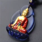 Tibetan Medicine Buddha Liuli crystal glass pendant with dark blue frame, gold gilt accents, red robed Buddha statue, and blue beaded silk cord