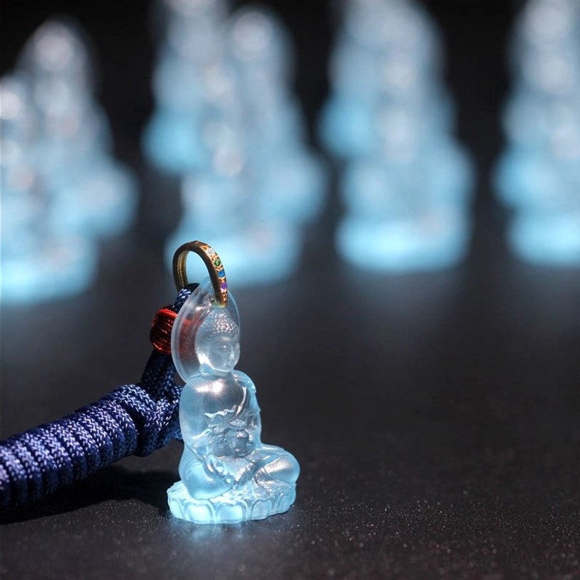 Single Medicine Buddha Liuli pendant on blue woven rope with red knot, front side view on dark black background, gem-studded metal bail detail