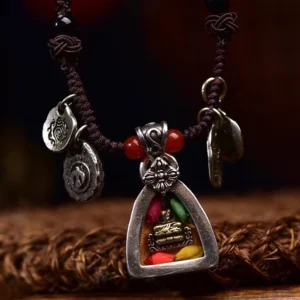 Close-up frontal view of Medicine Buddha silver amulet pendant featuring engraved healing buddha figure with red glass beads and silver floral clasp