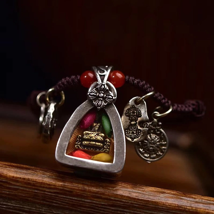 Front close-up of Medicine Buddha triangular pendant showing enclosed buddha figurine with colorful inner elements and silver floral clasp attachment