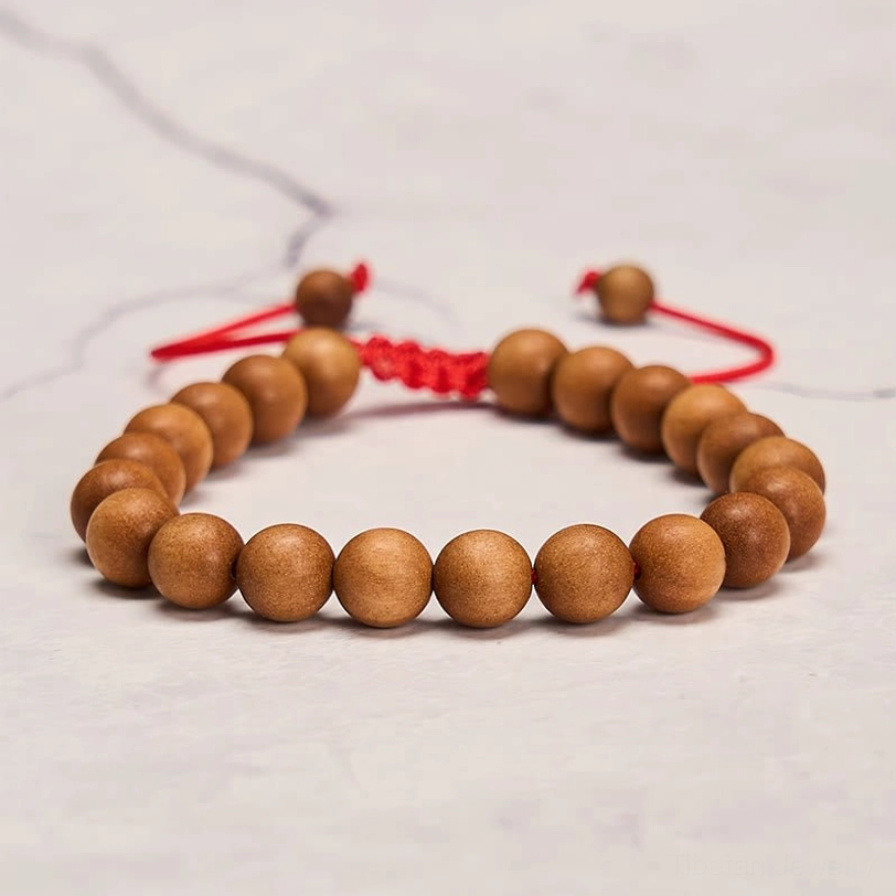 Meditation sandalwood mala bracelet side view on marble texture, smooth wooden beads with adjustable red tail cord