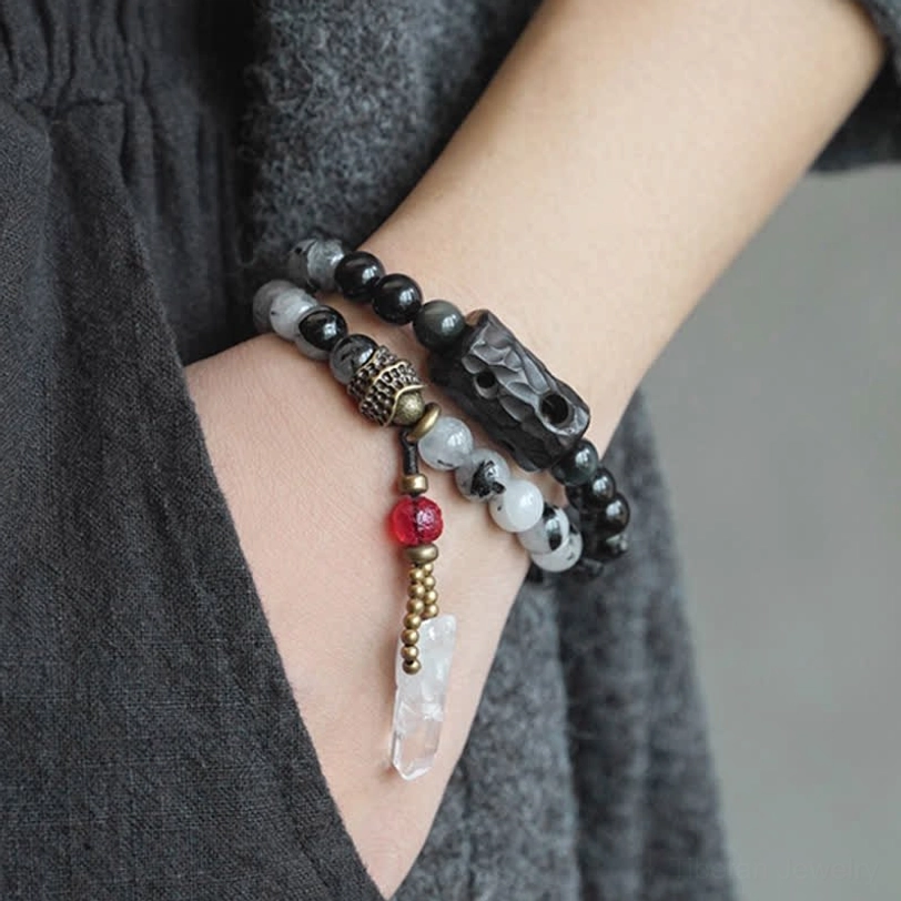 Men's black rutilated quartz couple bracelet worn on wrist with dark knit clothing close-up detail
