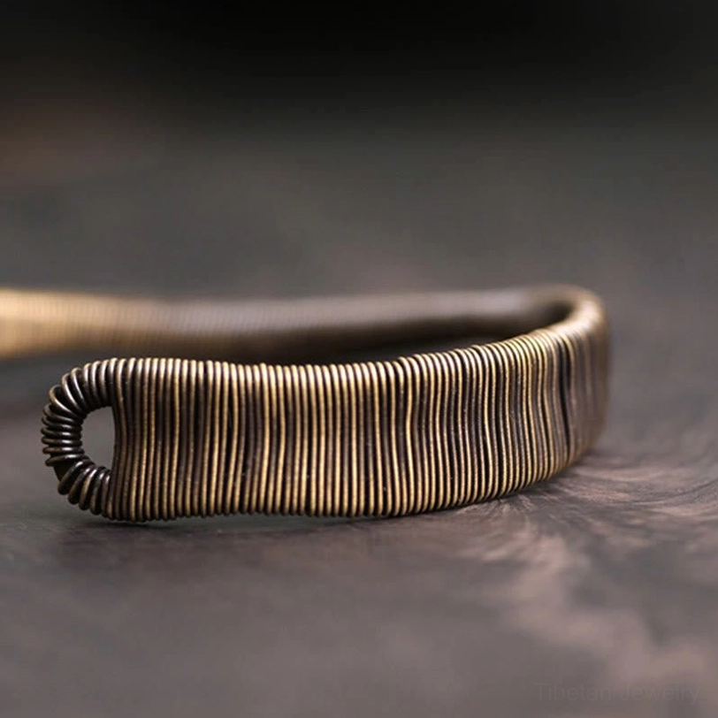 Slim wrapped wire band minimalist Tibetan cuff bracelet shown from top-down side view on dark wooden tabletop