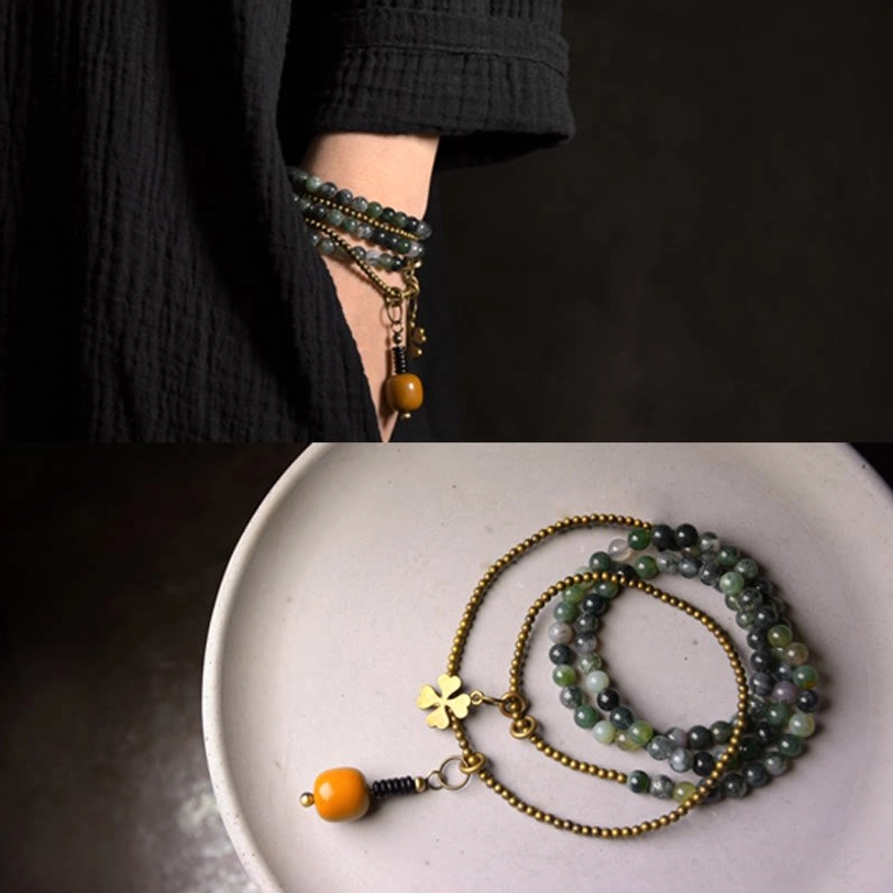 Compact stacked moss agate multilayer bracelet worn on model forearm against dark clothing background
