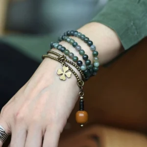 Moss Agate copper multilayer healing bracelet with four-leaf clover charm worn on female wrist, showing natural green stone beads and brass accents