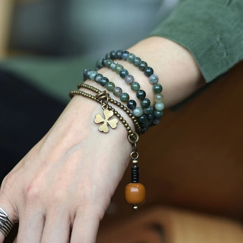 Moss Agate copper multilayer healing bracelet with four-leaf clover charm worn on female wrist, showing natural green stone beads and brass accents