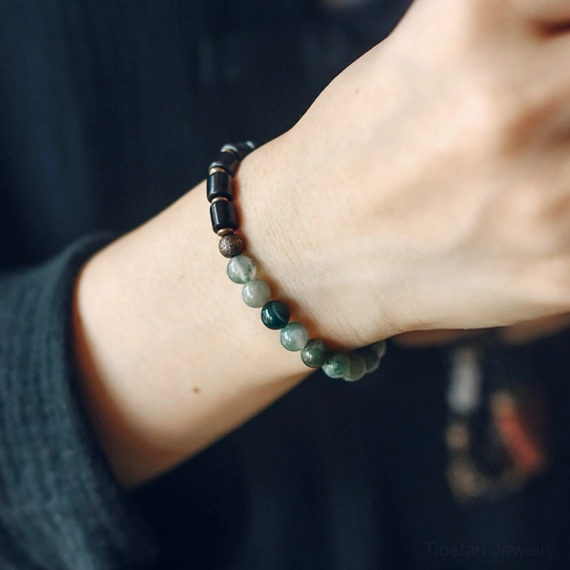 Minimalist moss agate and ebony bracelet worn on wrist showing comfortable everyday fit with dark fabric background