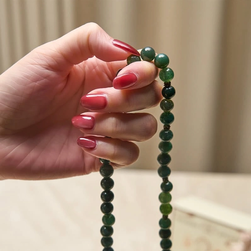 Hand-held moss agate mala strand with long bead chain and lotus charm, held up display close-up
