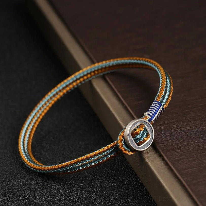 Multicolored woven tibetan bracelet side close-up showing intricate braided cord work with silver round buckle on wooden surface