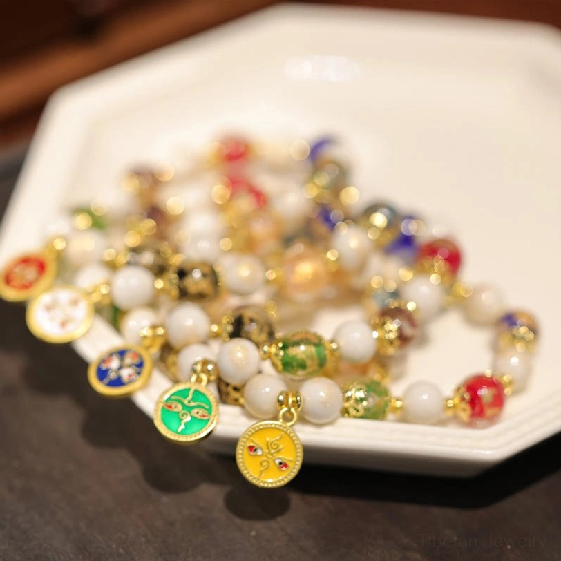 Multiple Five Gods of Wealth Tibetan bracelets arranged on ceramic plate displaying various colored enamel pendants and glass bead combinations