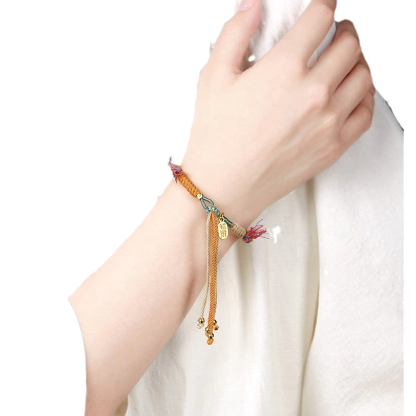 Tibetan Nafu luck bracelet worn on wrist with hanging long tassel and gold fortune charm on white background