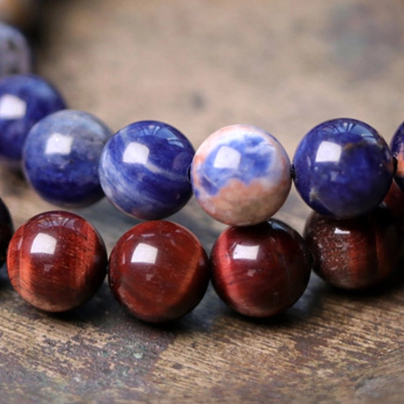 Polished blue Sodalite and red Tiger's Eye loose natural stone beads on wooden surface - raw materials for healing bracelet